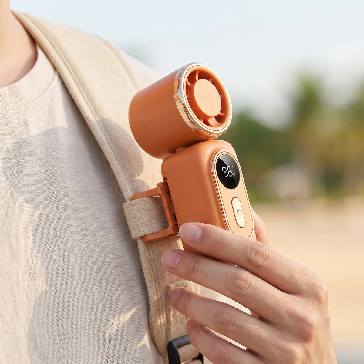 Ventilateur clip orange fixé sur la sangle d'un sac, tenu en main
