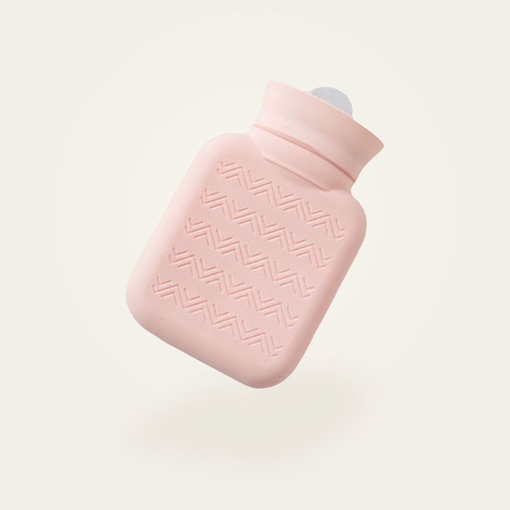 Bouillotte à eau en silicone rose, sans sa housse, fond crème